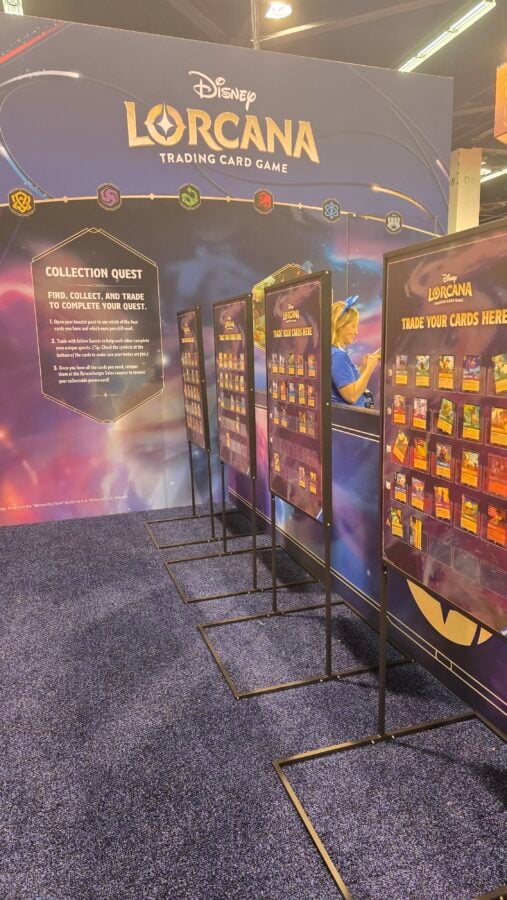 Disney Lorcana trading card game booth with a prominent Collection Quest panel and several card display boards along a purple backdrop