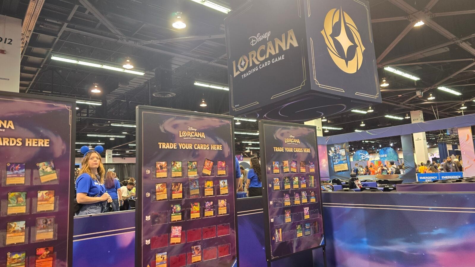 Disney Lorcana trading card game booth with tall blue banners and trade your cards signs attendees browsing card displays at a convention hall