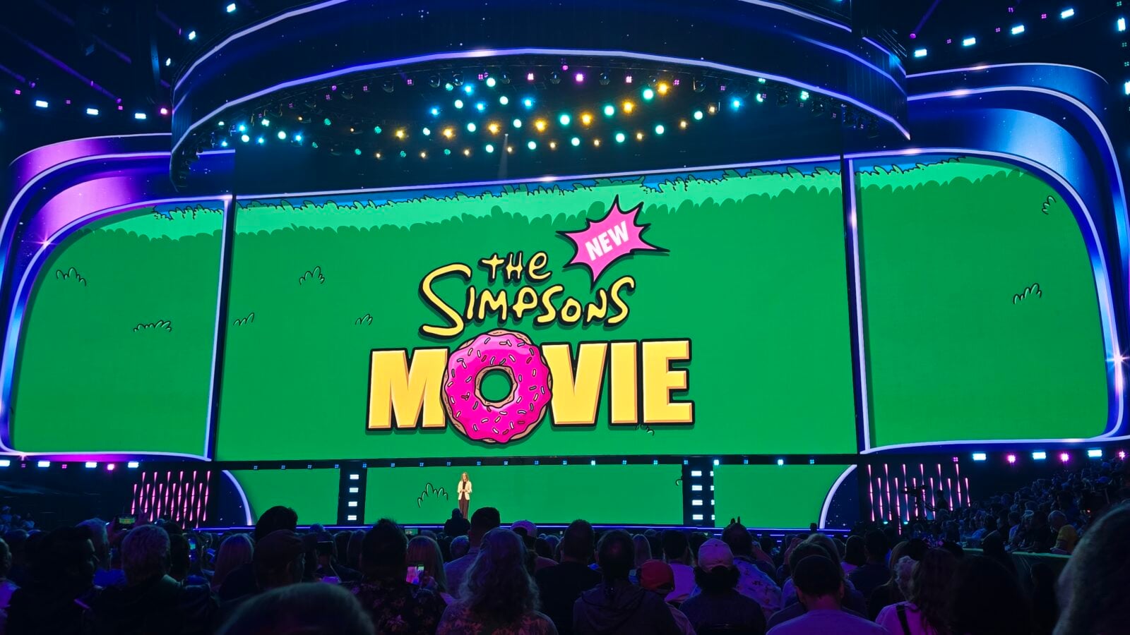 Stage with curved screens displaying The Simpsons Movie logo and a pink donut audience watching