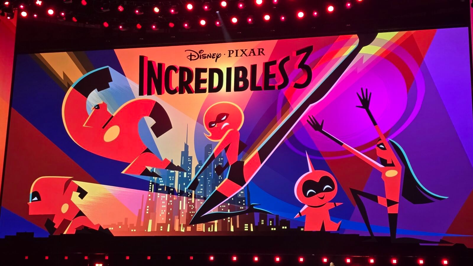Colorful stage backdrop promoting DisneyPixar Incredibles 3 with stylized superhero characters and cityscape art in bright red purple and orange hues