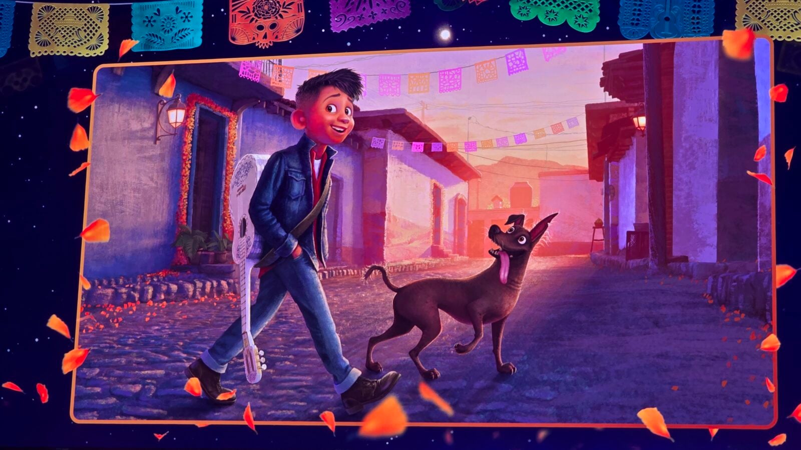 Cartoon boy with a guitar walking a large brown dog through a festive street lined with colorful papel picado banners