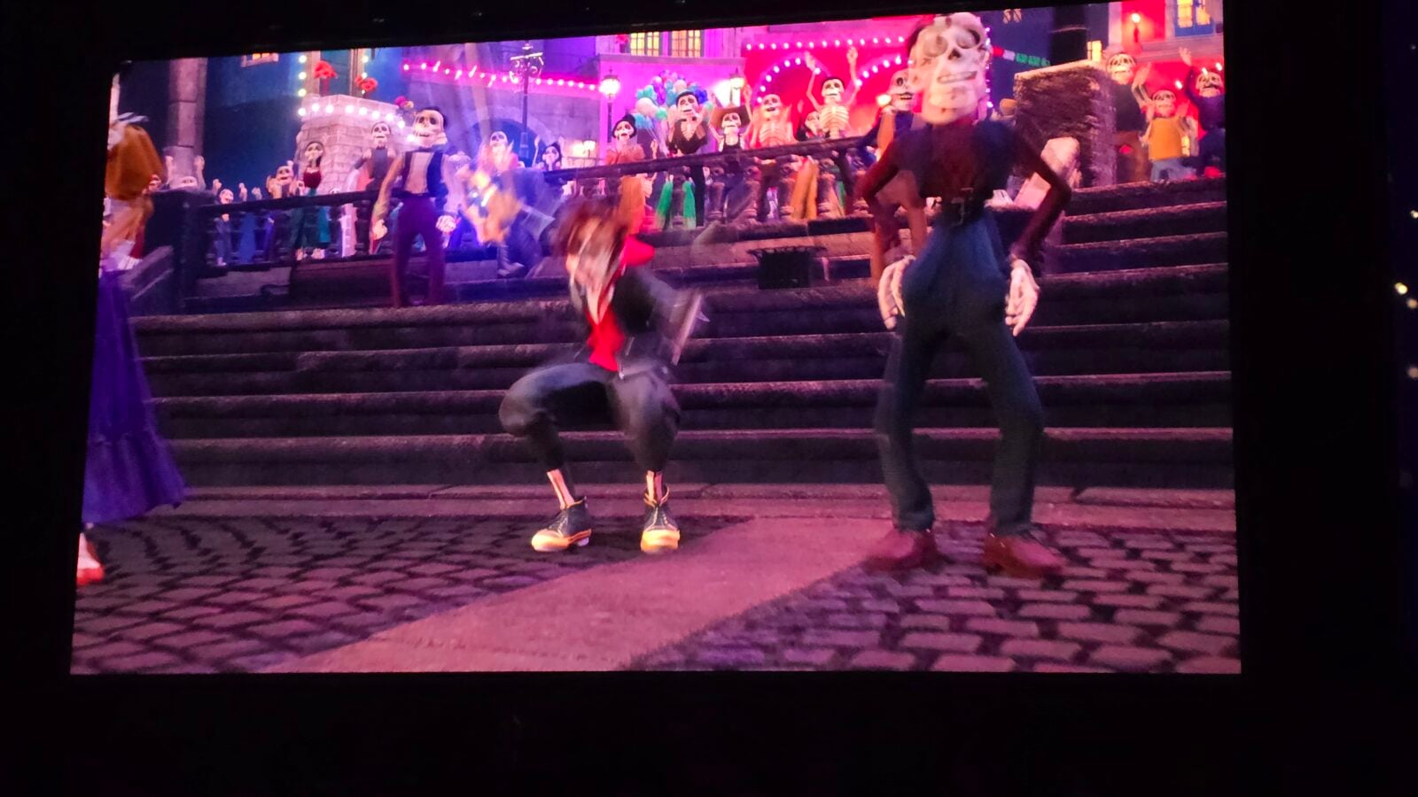 Theatrical stage scene with skeleton masked audience on stairs behind two dancers under colorful pinkpurple lights