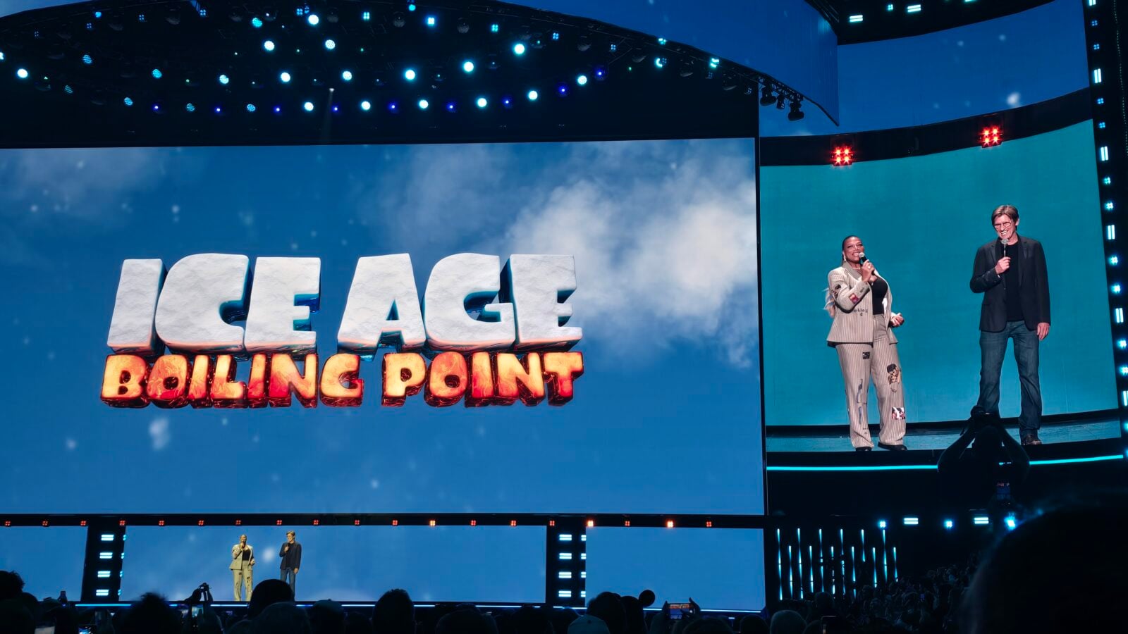 Two presenters stand on a lit stage beside a large 3D sign reading LEAGE BOLLING POINT against a blue cloudy backdrop