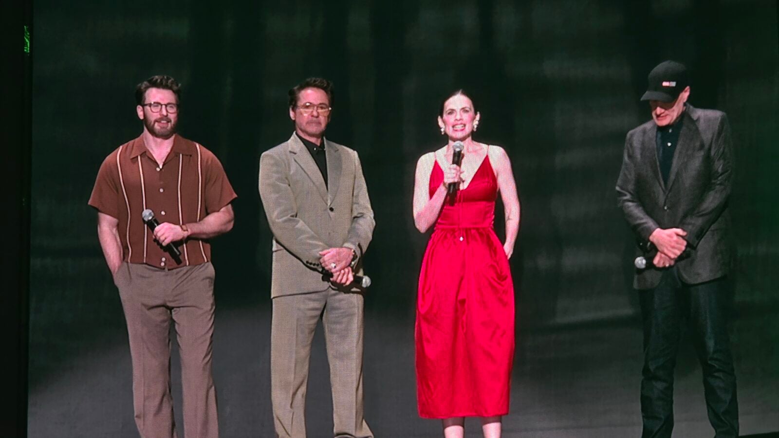 Four performers on a dim stage each holding a microphone standing in a row for a presentation or performance