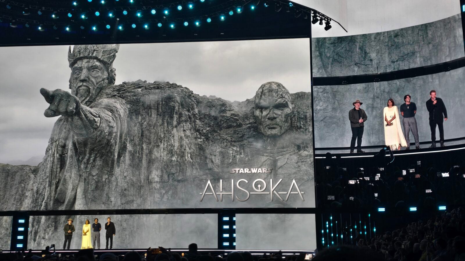 Large stage with a massive screen showing a stone statue from Star Wars Ahsoka panelists stand at right on the stage