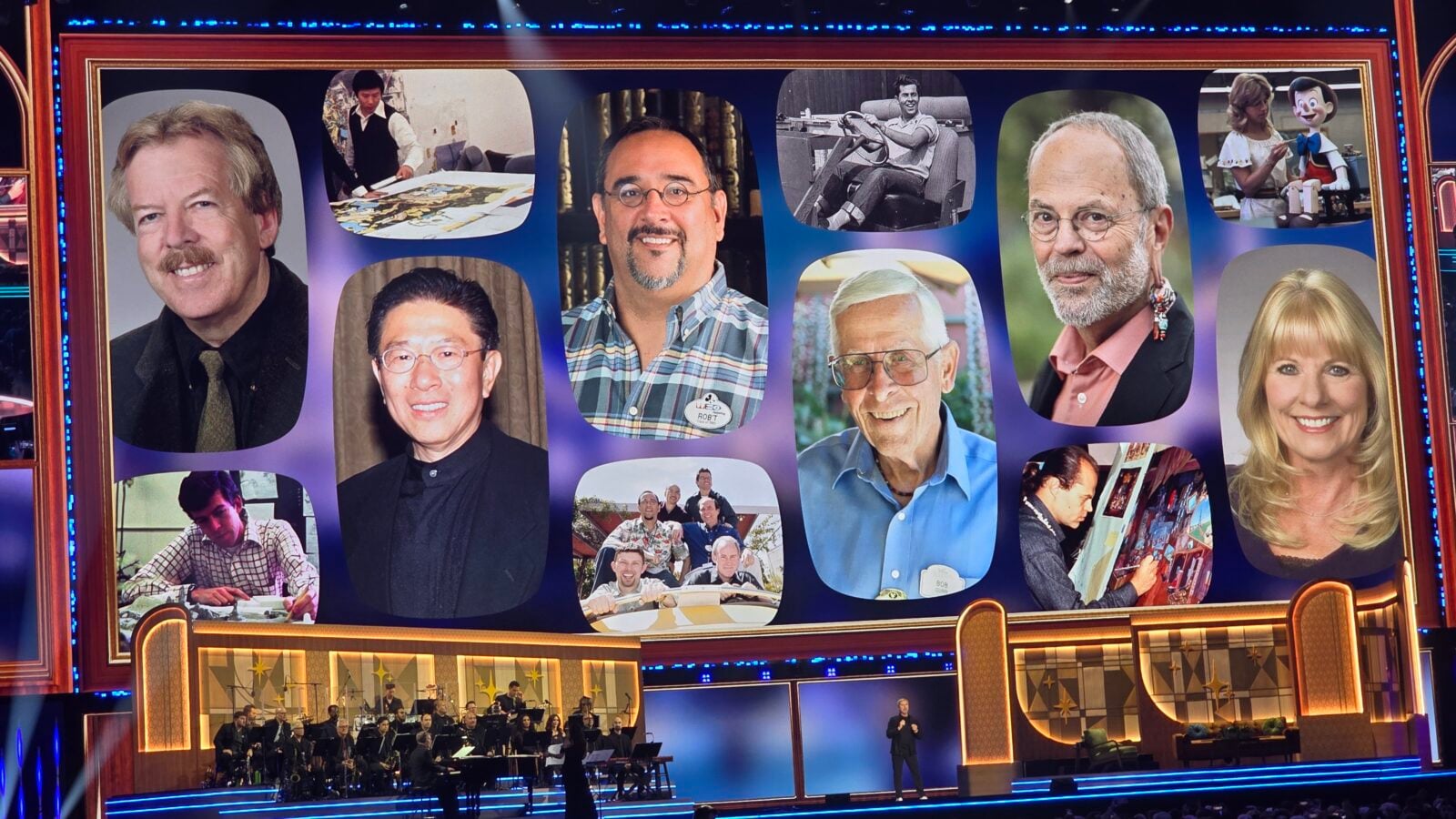 Stage backdrop with a collage of portrait photos above a live orchestra performing on a theater stage