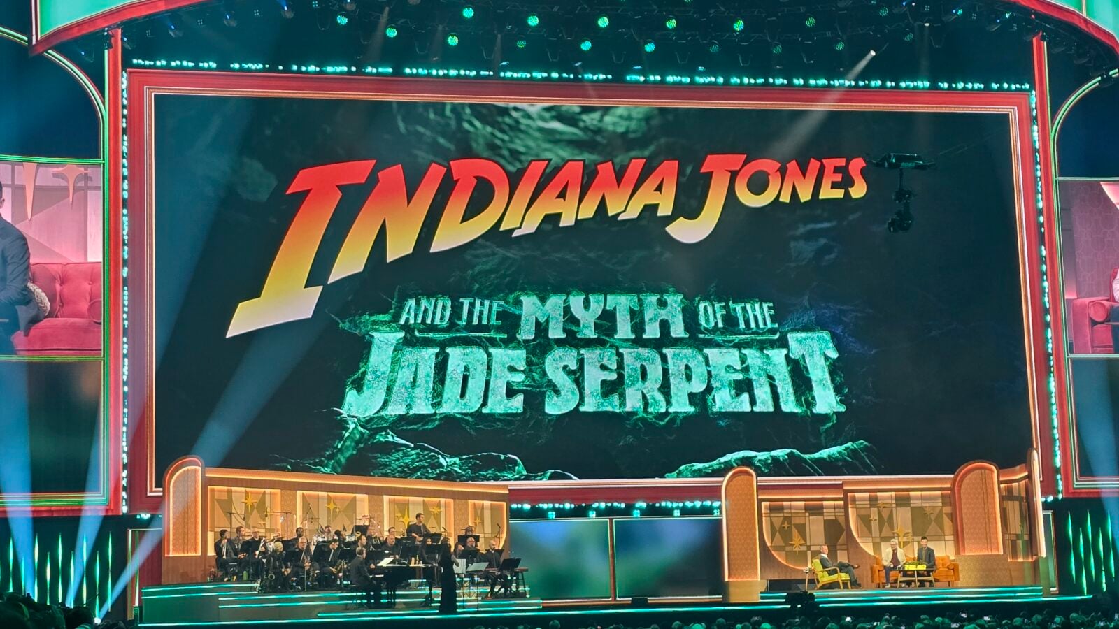 Stage with a large screen reading Indiana Jones and the Mystery of the Jade Serpent and an orchestra performing below it