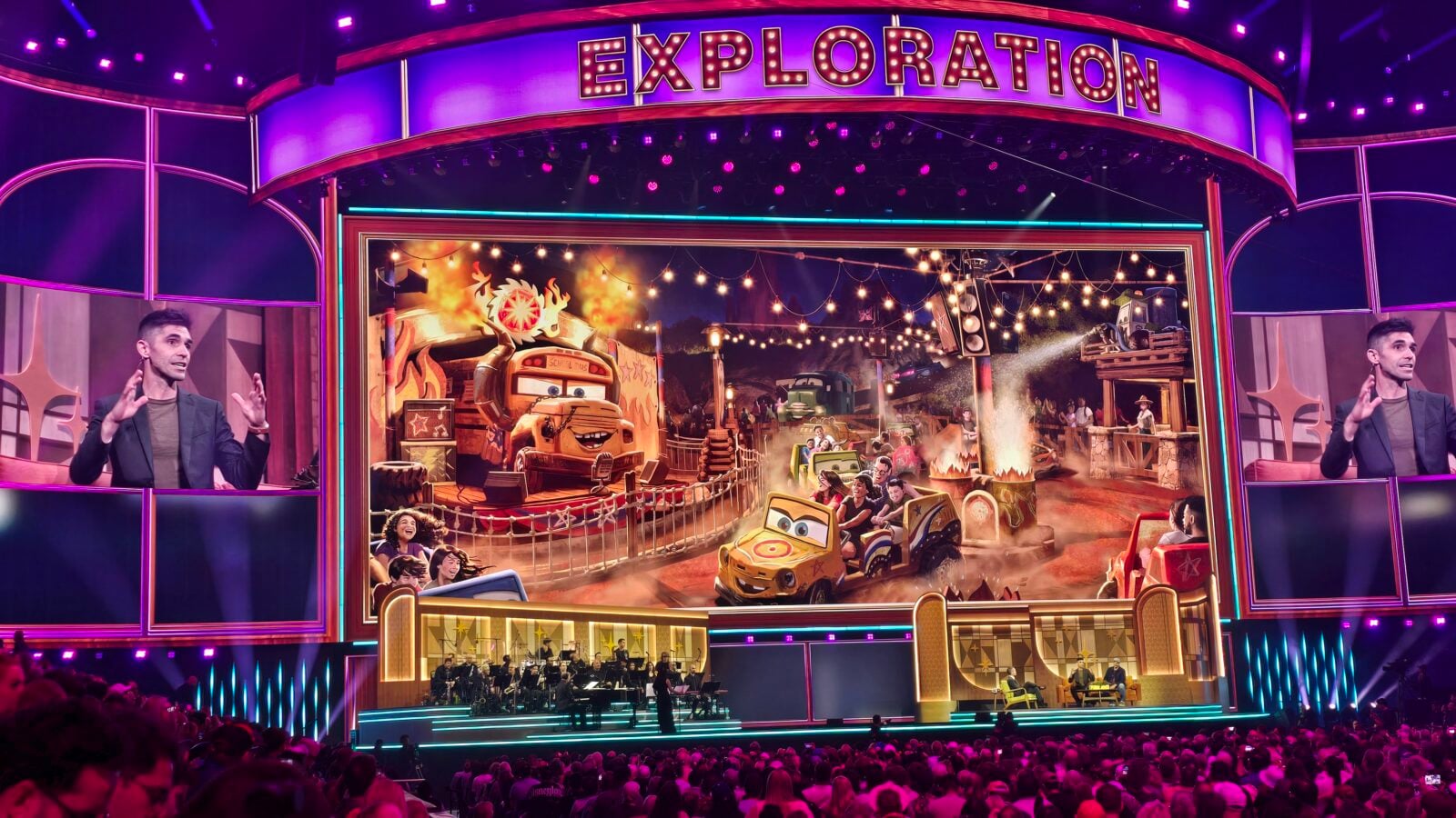 Theater stage with a bright EXPLORATION sign a colorful Cars themed ride backdrop string lights and an orchestra performing below a seated audience