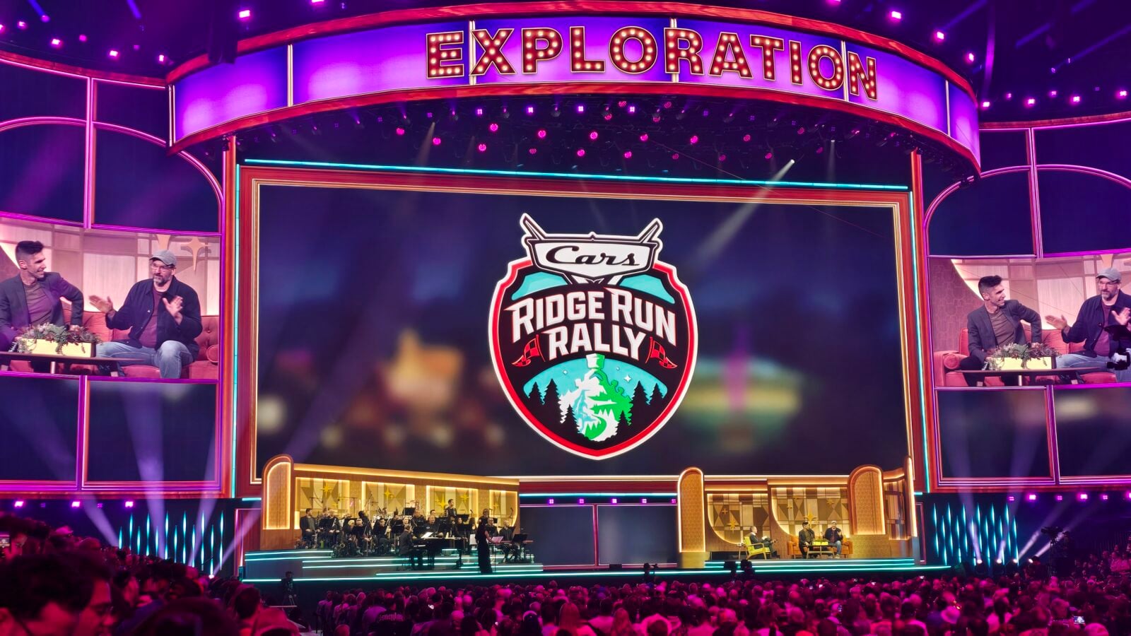 Vibrant stage with a bright EXPLORATION sign above a large Ridge Run Rally logo on a central screen and hosts seated on both sides amid audience
