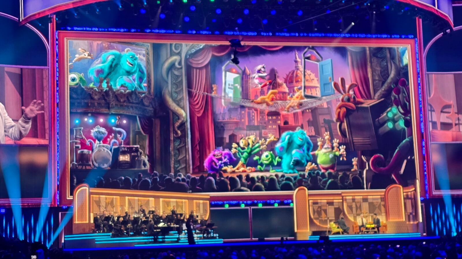Colorful monster themed stage show with performers and an orchestra in front audience watching a large illuminated theater set