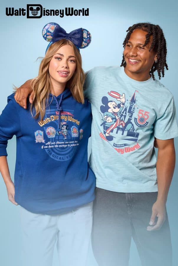 Two friends posing in Disney World apparel against a blue background woman wears a blue hoodie with Minnie ears man wears a light blue shirt with Mickey designs and 55th logo