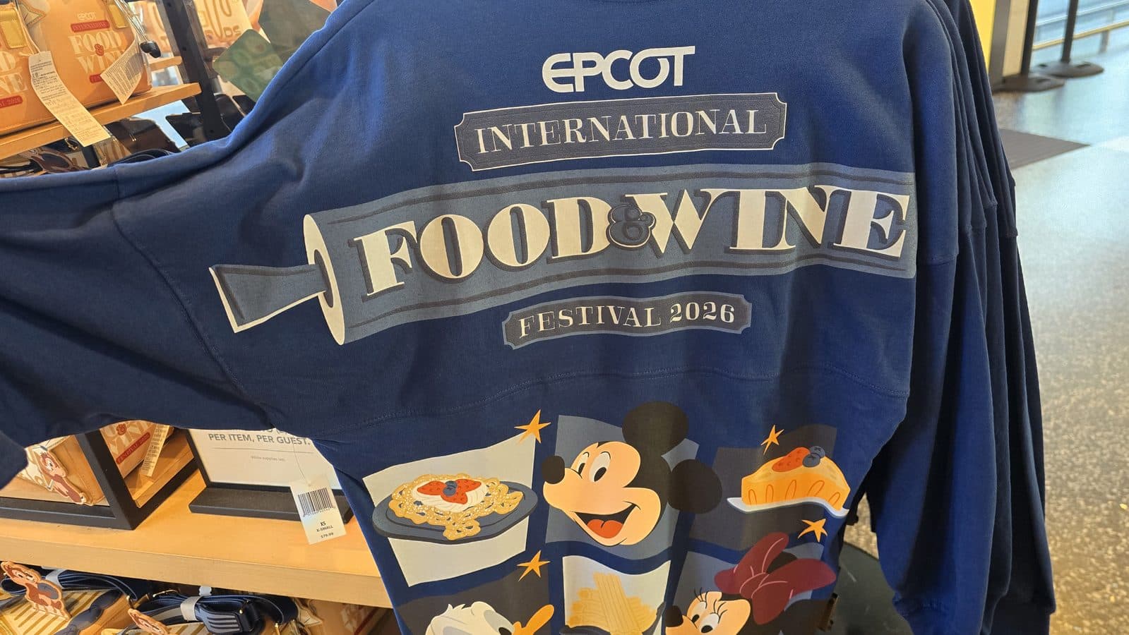 Blue festival themed T shirt with EPCOT INTERNATIONAL and FOOD  WINE FESTIVAL 2026 graphics on display