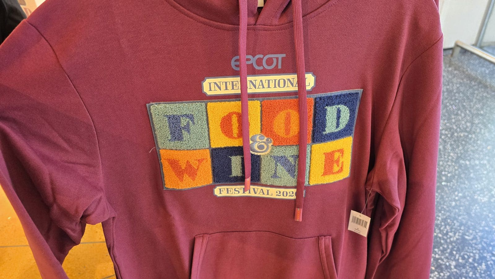 Maroon hoodie with a colorful patch reading INTERNATIONAL and FESTIVAL 2020 a pink lanyard hanging over the chest