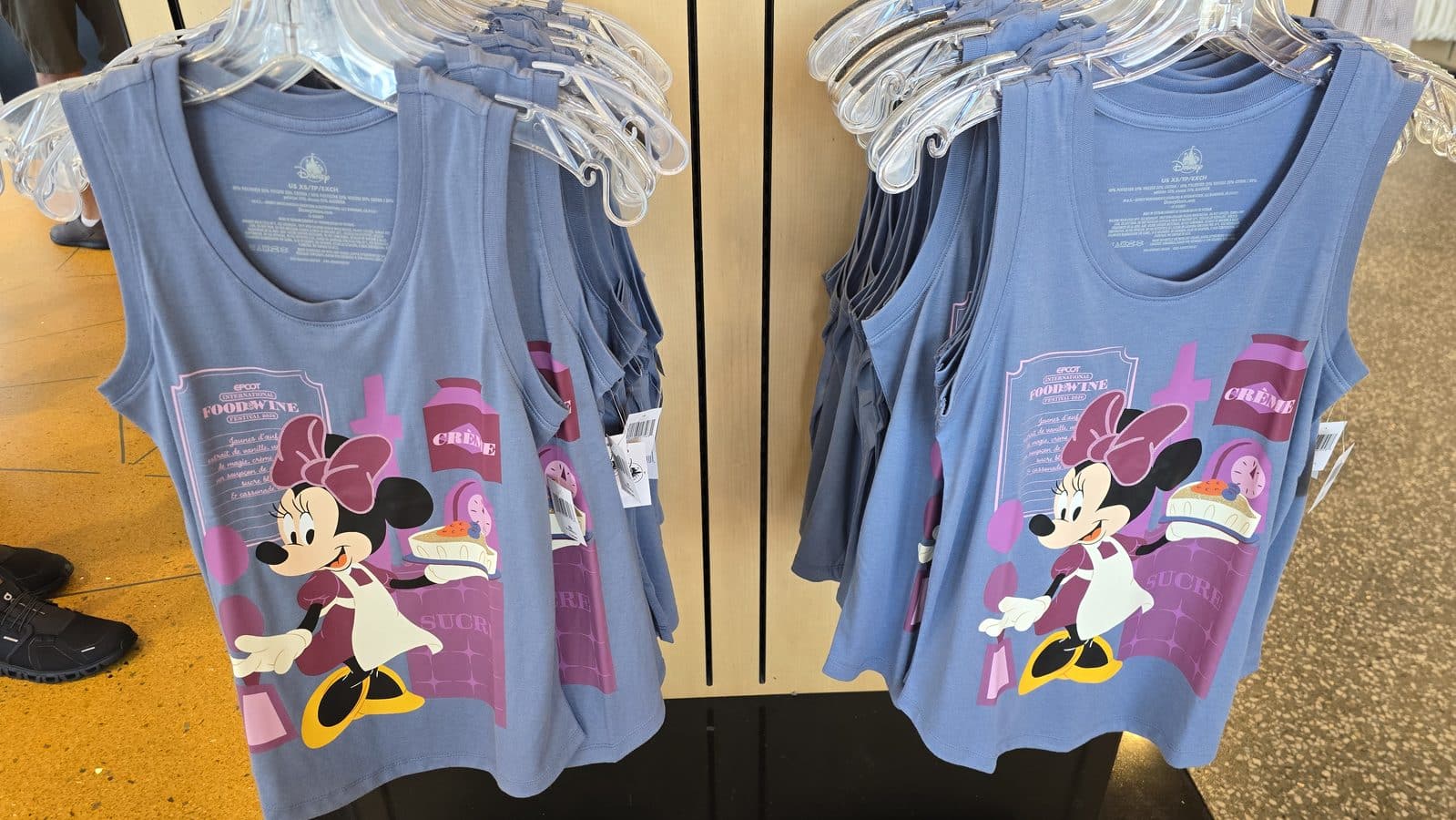 Blue sleeveless shirts with Minnie Mouse and cake graphic hanging on a clothing rack in a store display
