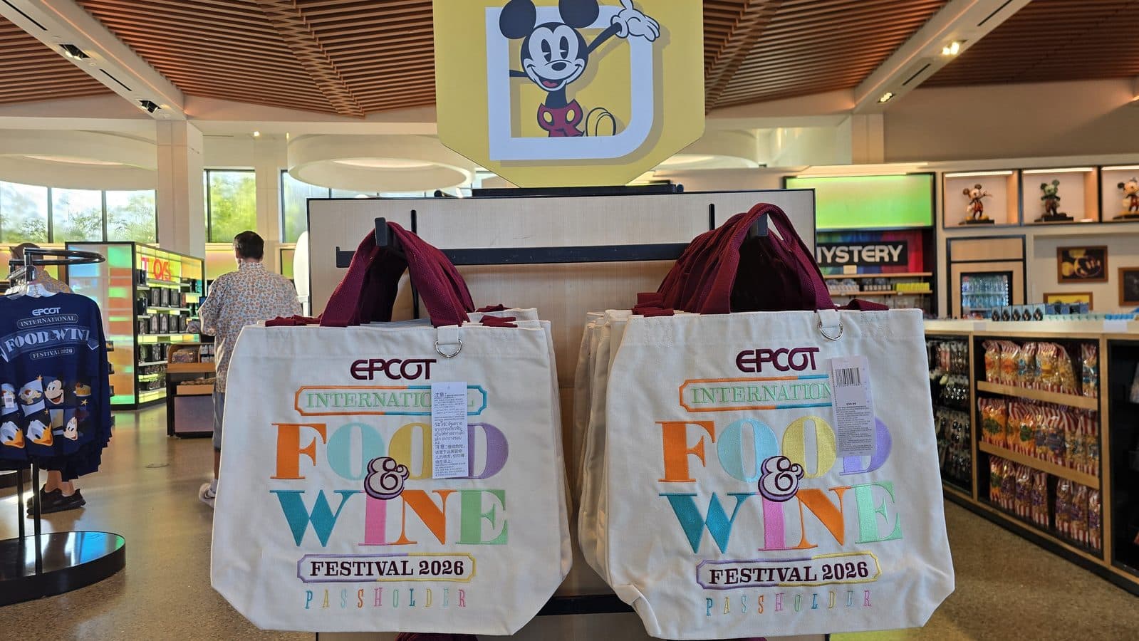 Two white tote bags with colorful EPCOT International Food  Wine Festival 2026 text hanging in a souvenir shop display