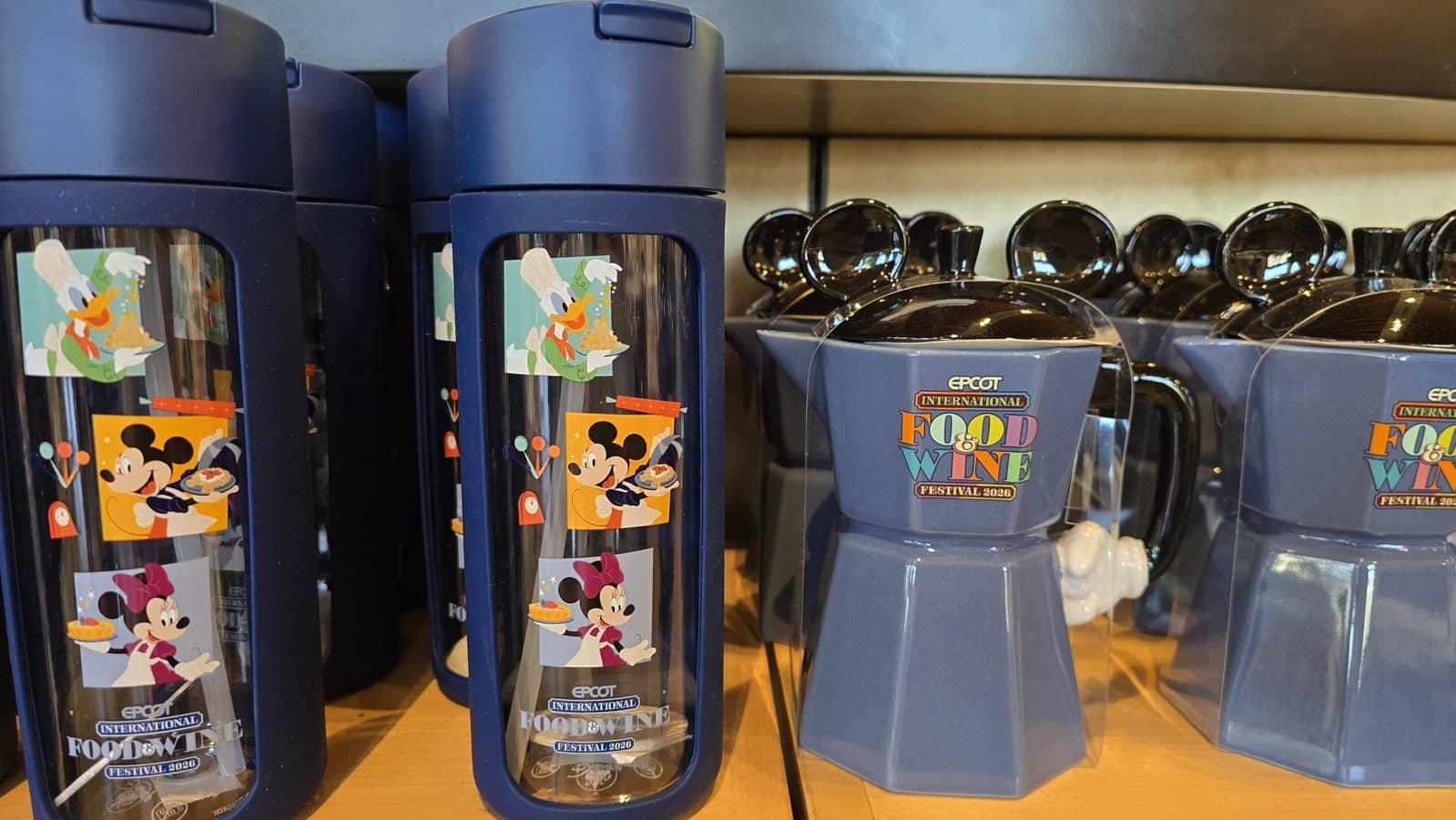 Blue stainless steel travel mugs on a display adorned with Disney characters and a Food  Wine Festival 2026 sticker