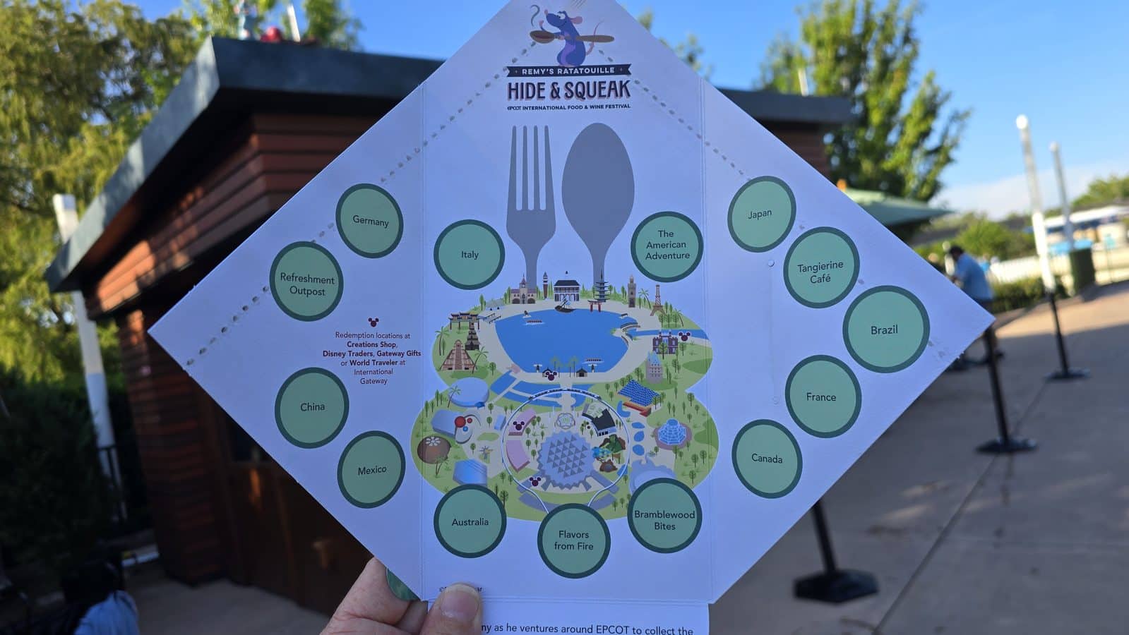Pyramid shaped map brochure for an EPCOT food festival with green circular country markers around a central illustrated world map held outdoors by a person