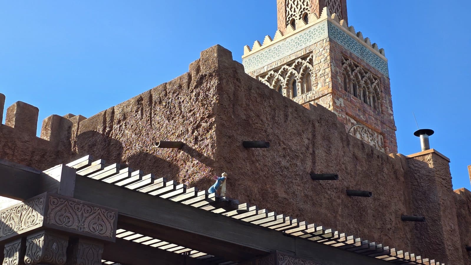 Adobe wall with decorative carvings and a brick tower with arched windows under a clear blue sky Southwestern style building featuring a turquoise tile band and arched windows atop brown textured walls