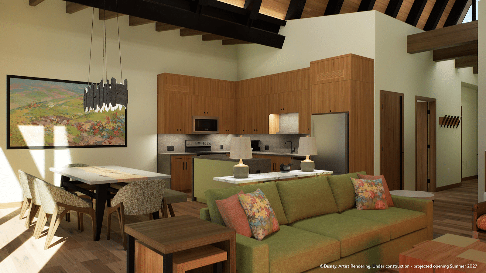 Open concept living area with a green sofa wood kitchen cabinets and a dining table under exposed dark wooden beams