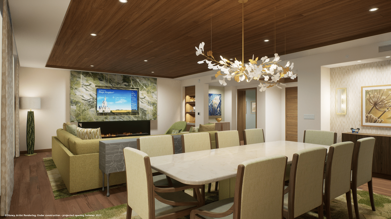 Modern hotel living room with a long dining table beige chairs and a wood paneled ceiling chandelier in the center of the room A fireplace and TV are on the far wall