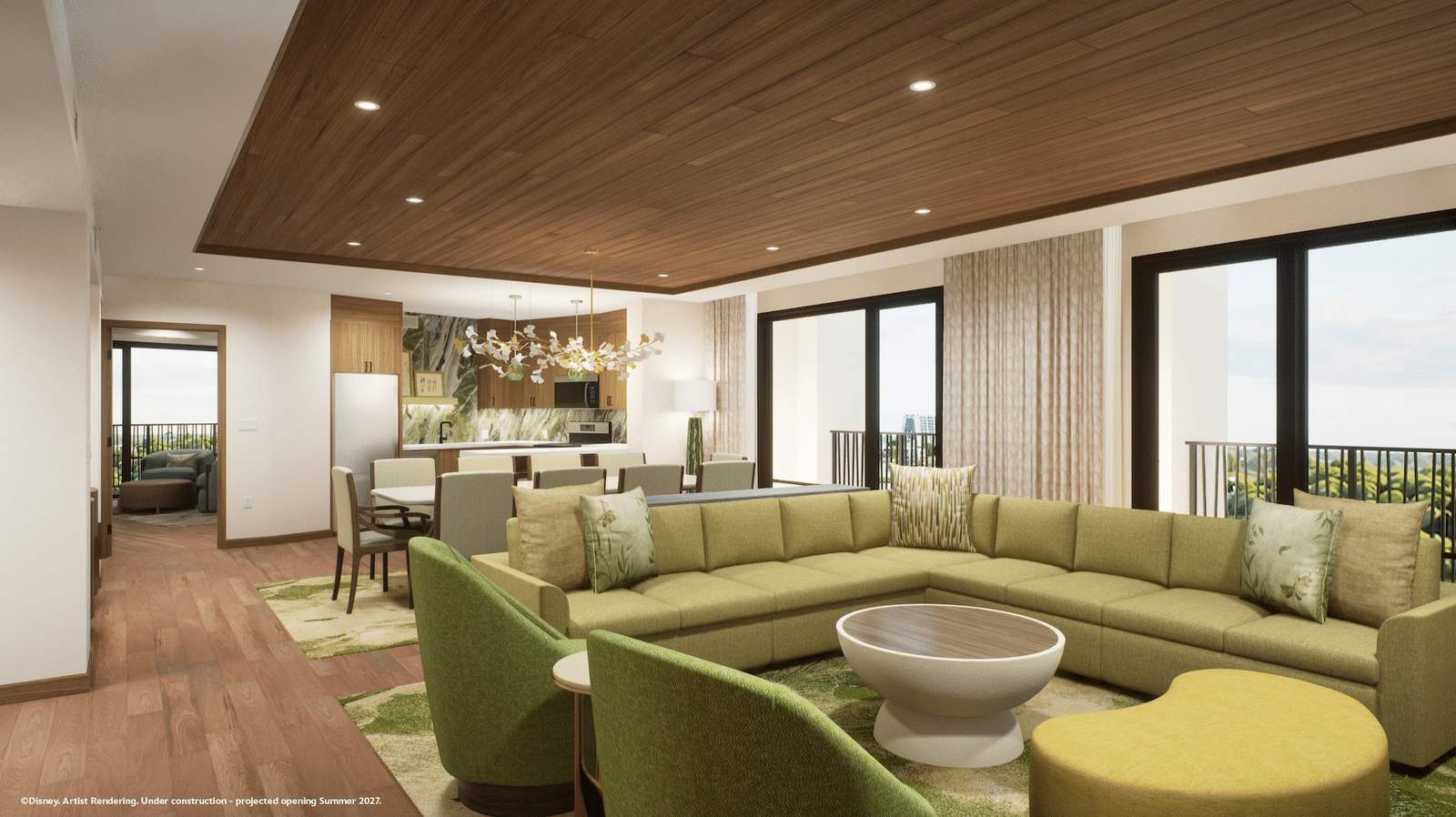 Open concept living room with olive green sectional yellow ottomans and a kitchen area in the background under a wood paneled ceiling