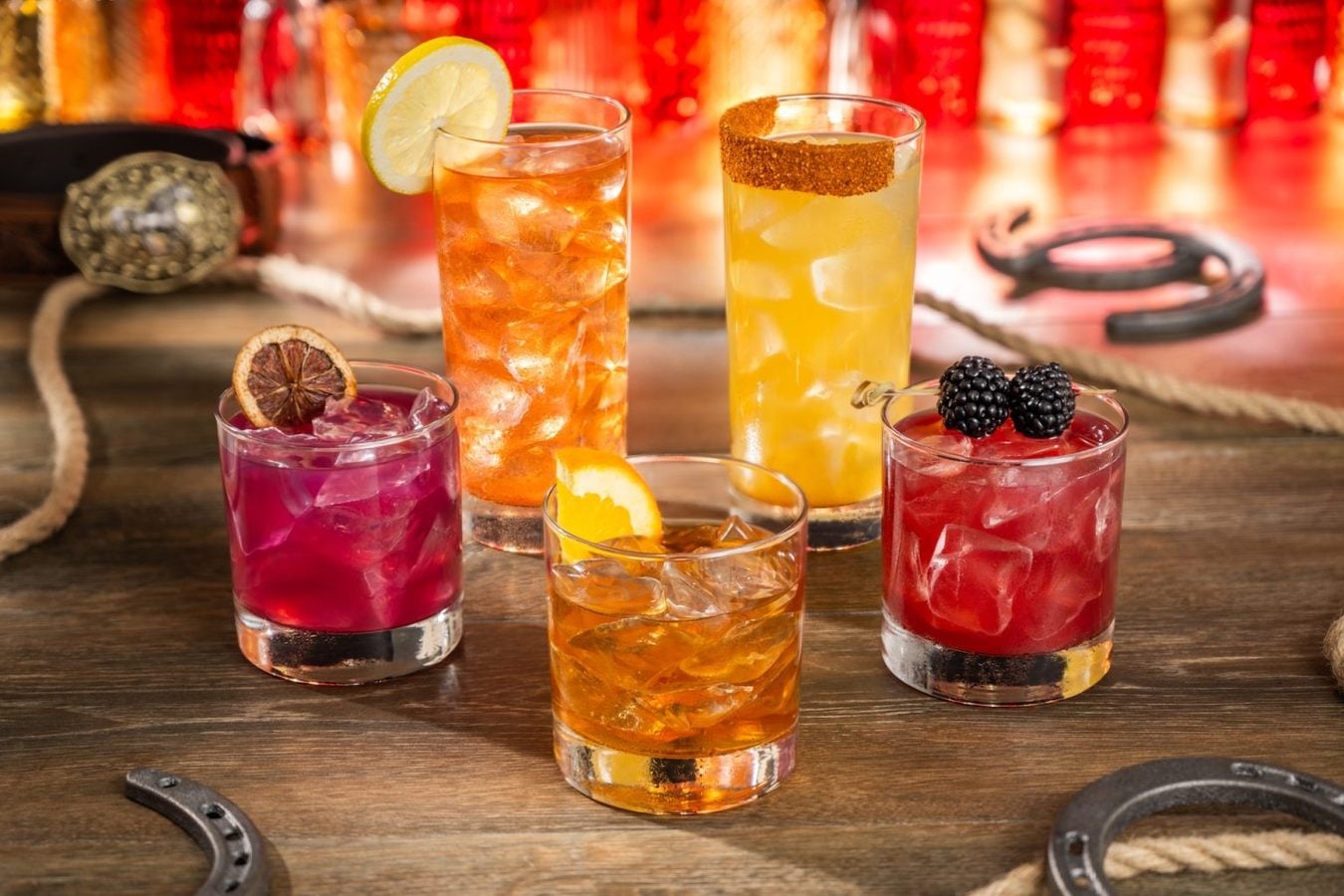 Six colorful cocktails on a wooden bar each iced and garnished with citrus berries or a sugar rim