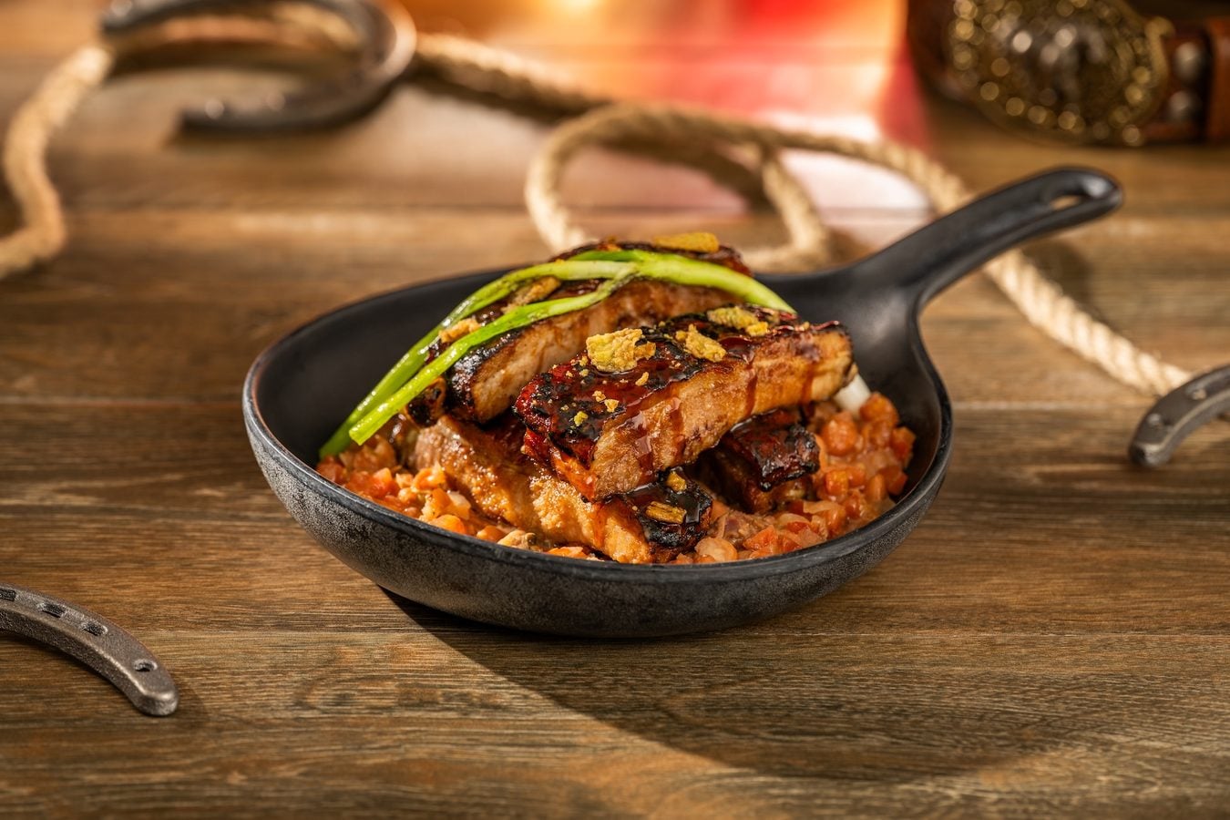 Cast iron skillet with glazed grilled pork ribs atop a tomato bean ragout garnished with green onions