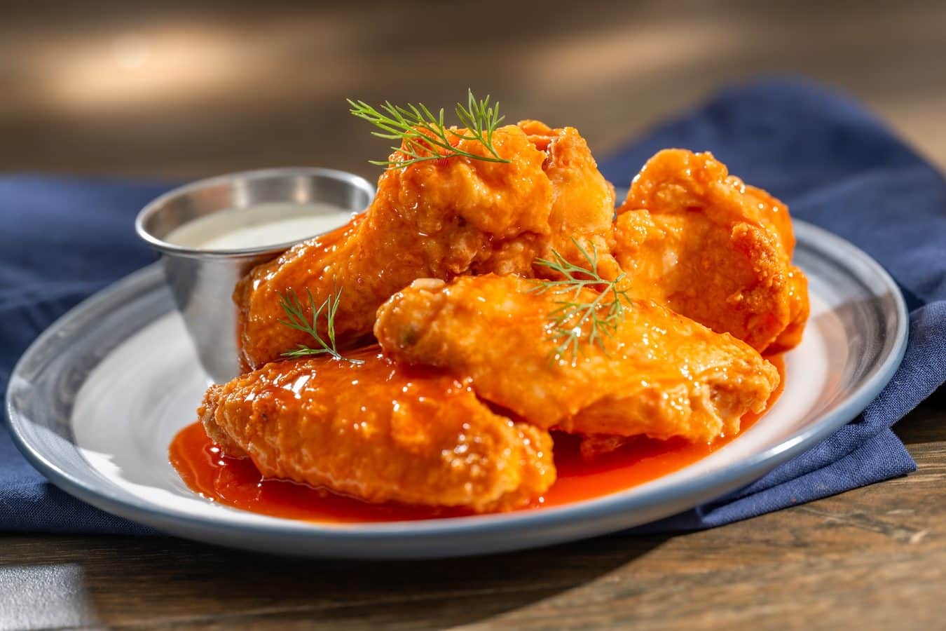 Plate of buffalo style chicken wings coated in orange sauce with dill sprigs and a ramekin of ranch on the side