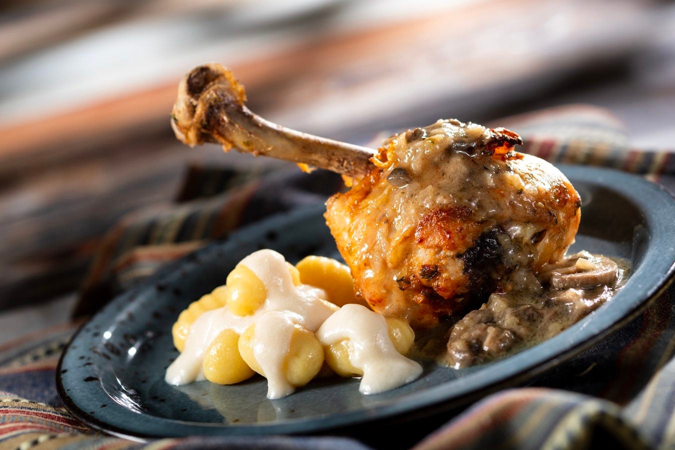Roasted chicken leg with melted gravy on a plate accompanied by creamy corn and mashed potato like dumplings