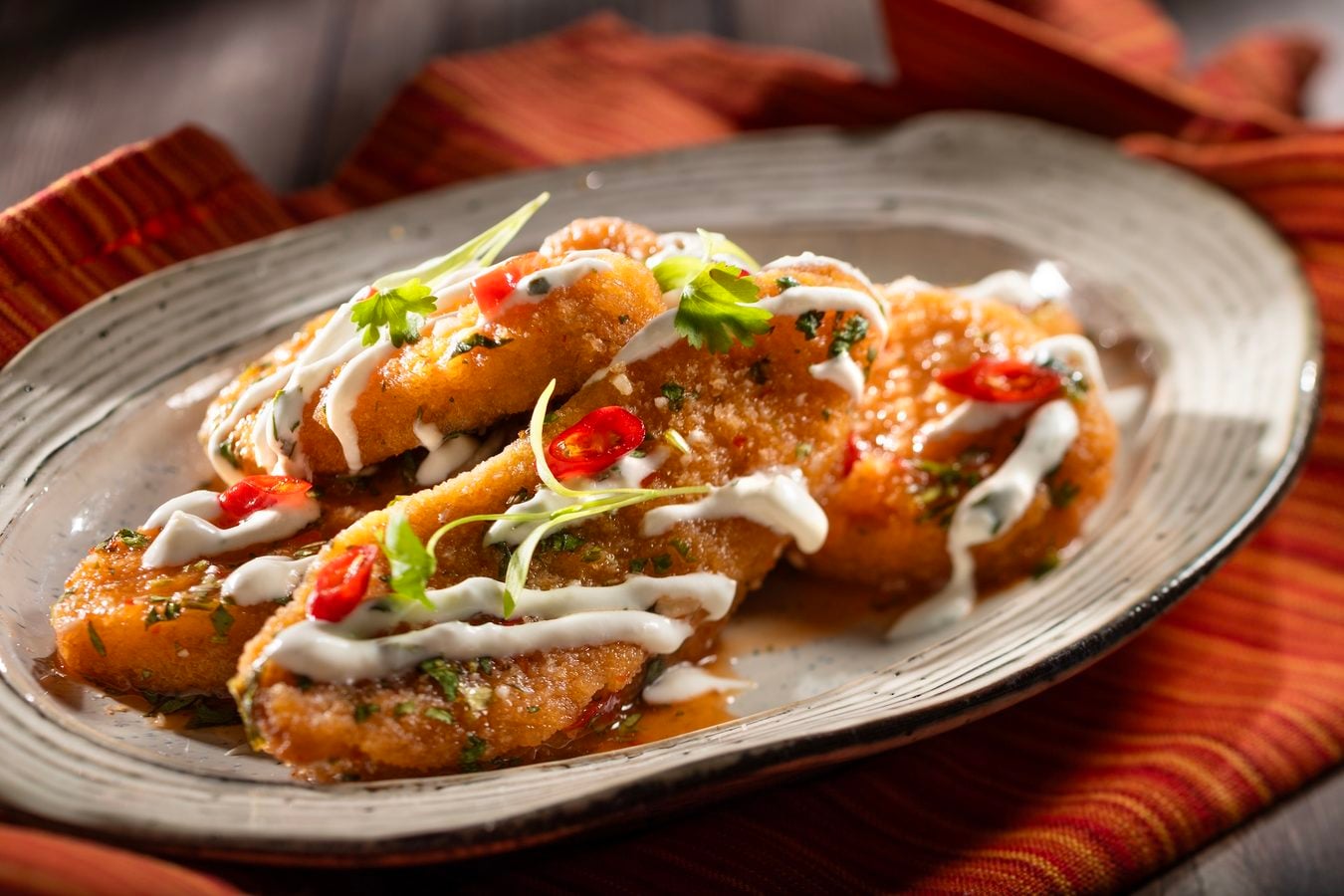 Crispy fried fish bites with white sauce red chili and chopped herbs on a decorative plate