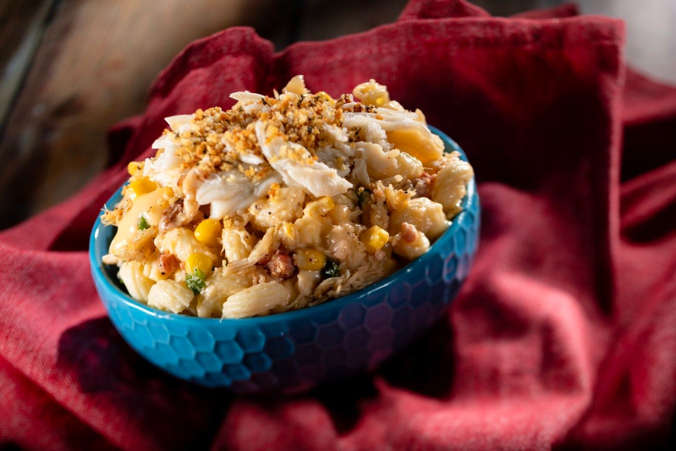 Blue bowl of creamy chicken pasta salad with corn on a red cloth background close up view vibrant colors