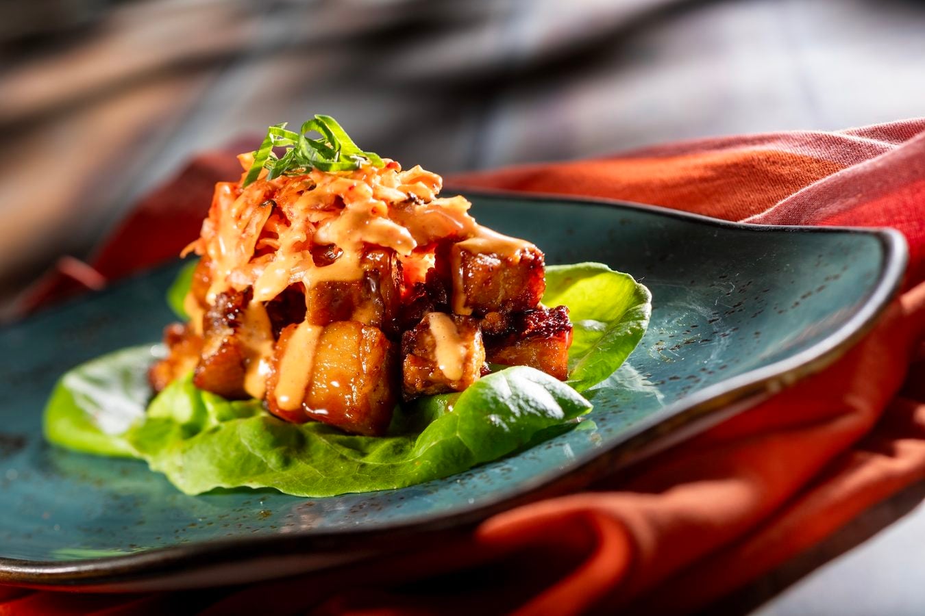 Stacked pork belly with a creamy glaze on a bed of greens topped with green onion curls