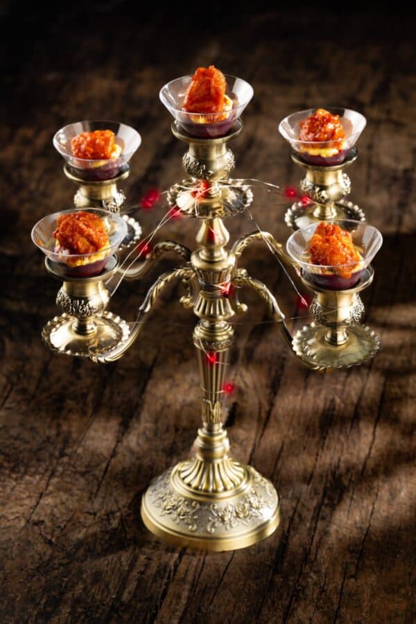 Brass multi arm candelabrum with glass bowls holding red trosted desserts on a wooden table