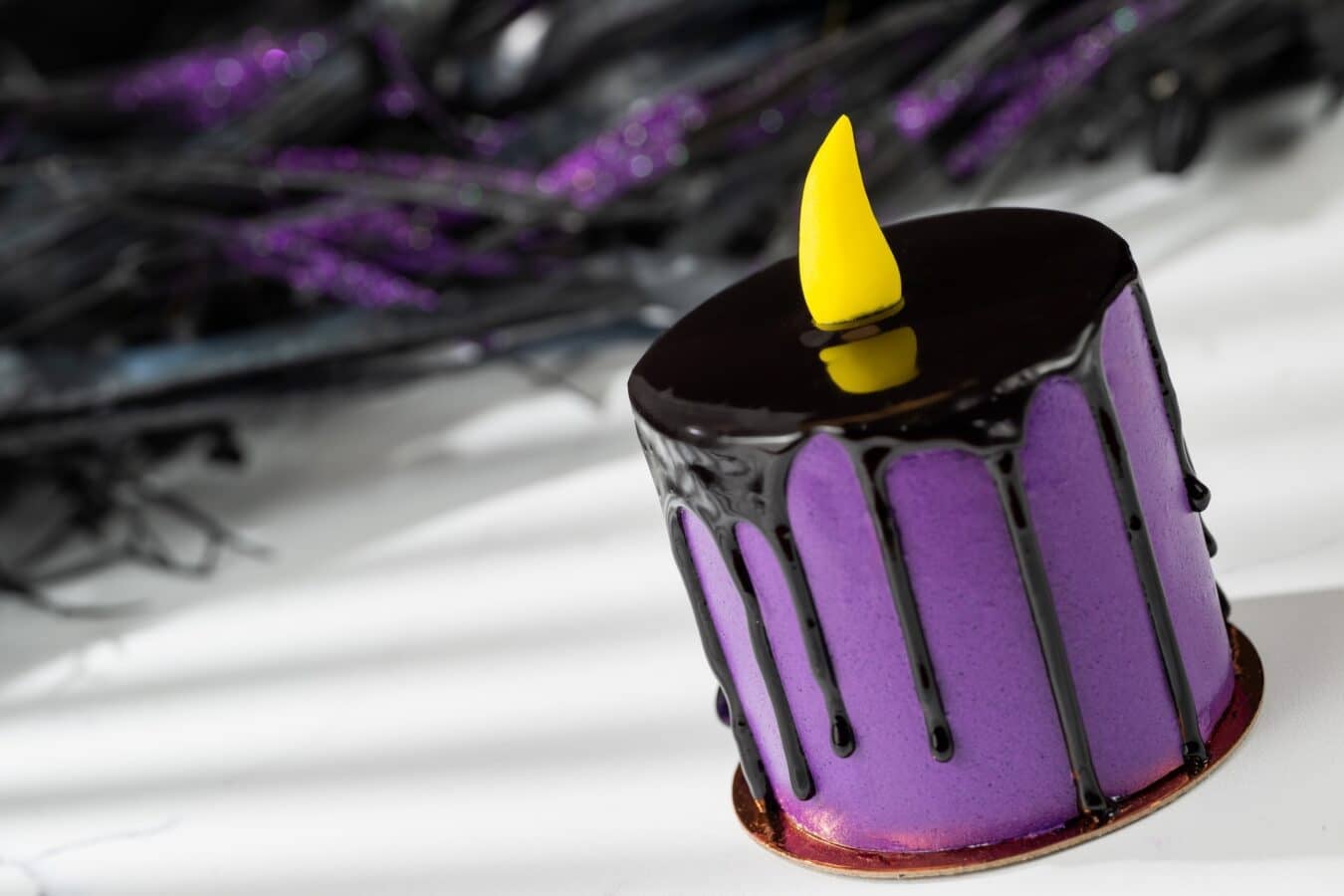Close up of a purple frosted cake with glossy chocolate glaze and a yellow fondant decoration on top