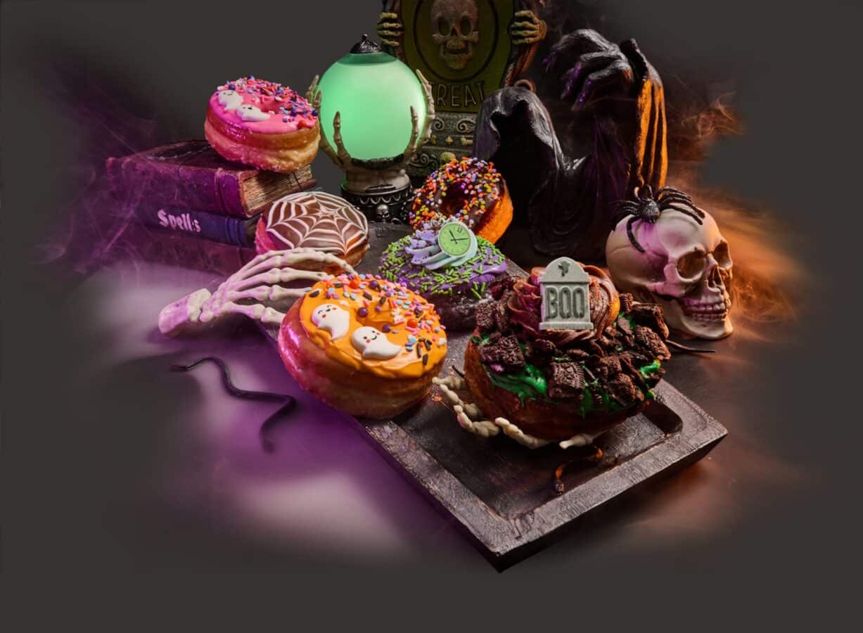 Assortment of Halloween donuts with colorful icing and sprinkles on a wooden board with a skull and spooky props in the background