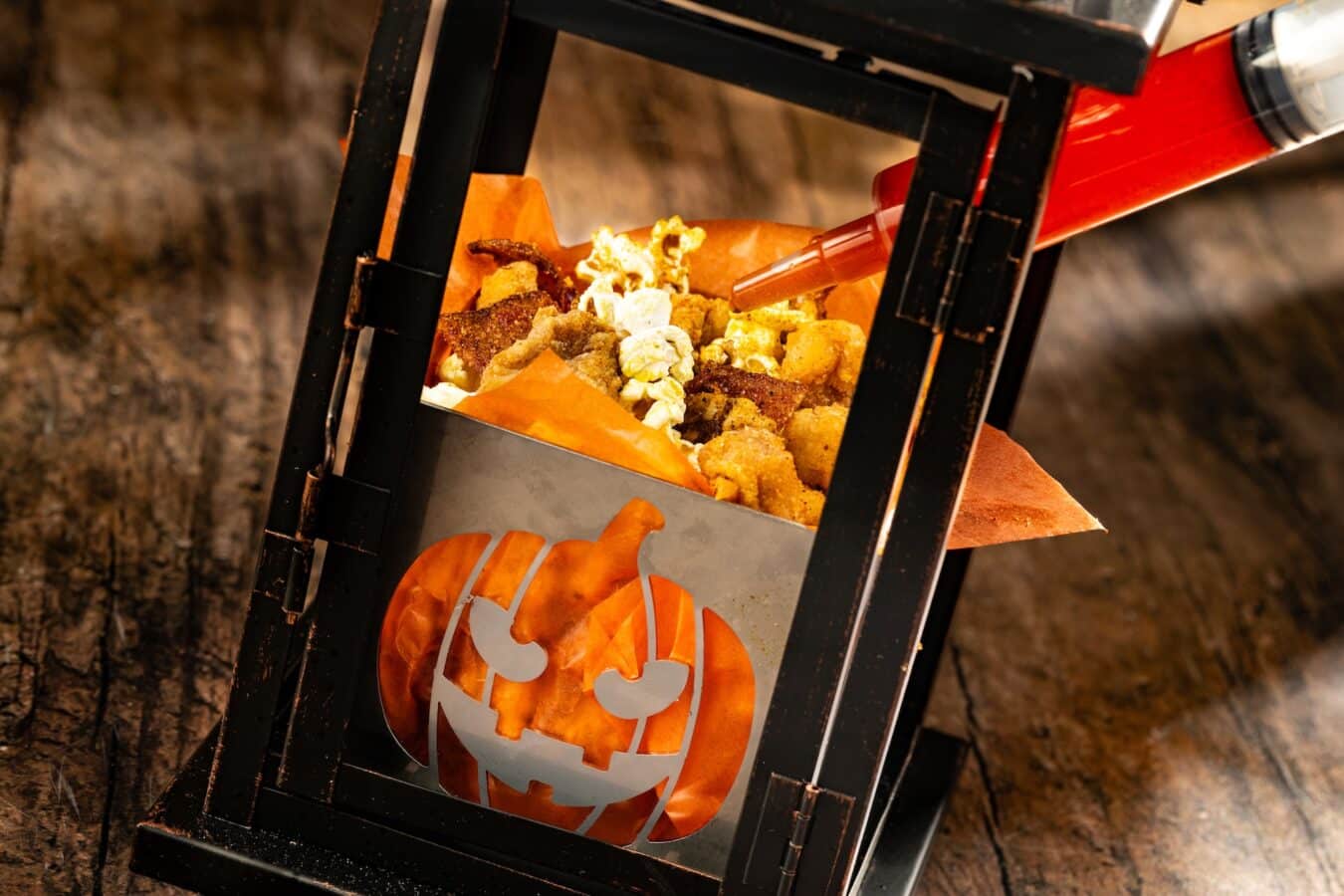 Close up of an orange Halloween bag overflowing with popcorn inside a black metal frame on a wooden surface