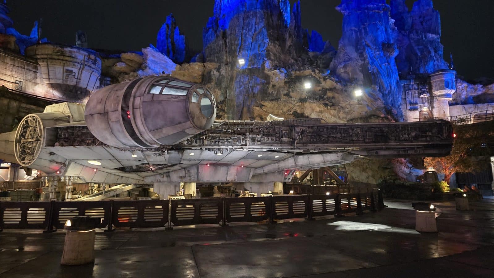 Millennium Falcon replica on a raised platform at night with blue lit rock formations in the background