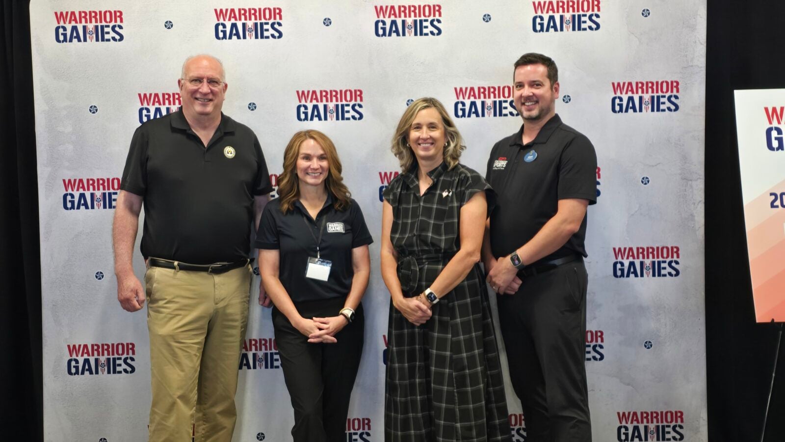 Four people smiling and posing for a photo in front of a Warrior Games backdrop