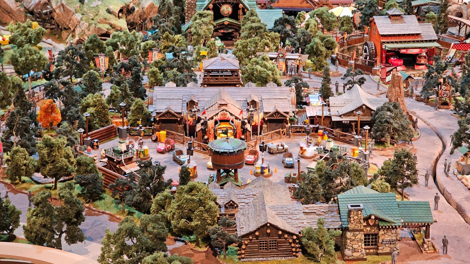 Wide view of a miniature amusement park town with wooden buildings trees and tiny cars scattered around