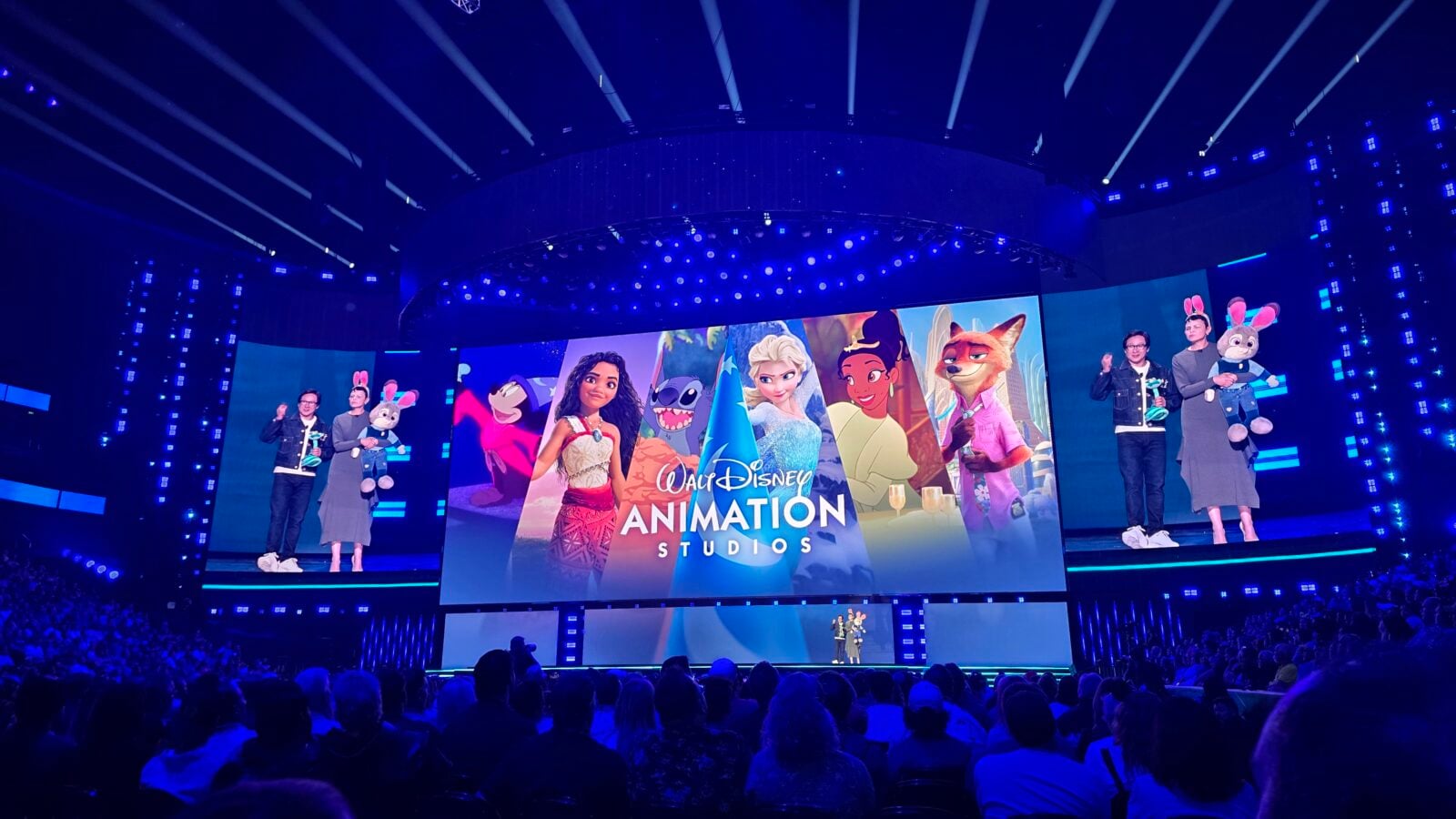 Stage presentation at Walt Disney Animation Studios with performers and large screens displaying animated characters blue dramatic lighting