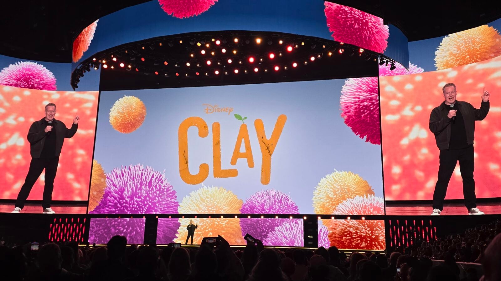 Two men on a colorful stage with a large screen that reads PLAY and fireworks graphics behind them