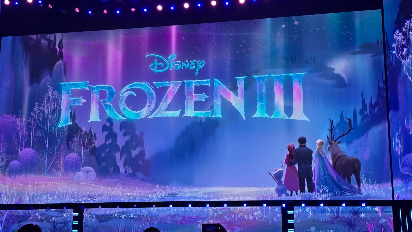 Disney Frozen II stage backdrop with a blue icy title and silhouettes of characters in a snowy forest setting