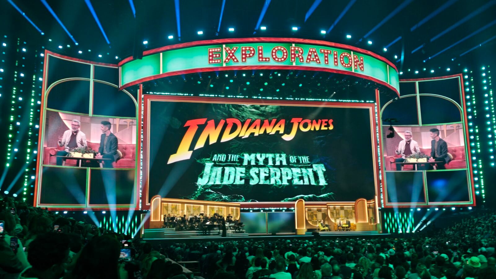 Large theater stage with a green neon EXPLORATION sign and a central screen announcing Indiana Jones and the Myth of the Jade Serpent during a live show