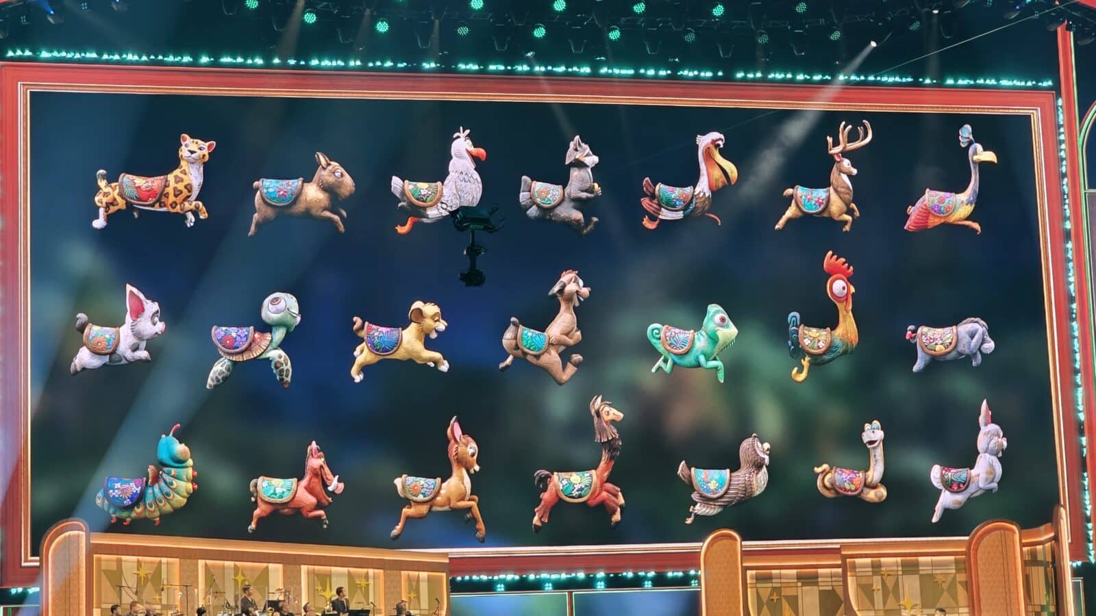 Colorful animal puppets suspended in midair on a theater stage framed by bright lights and a decorative border as part of a performance