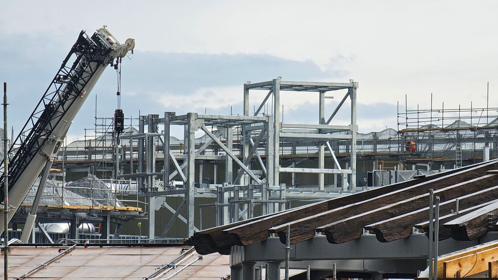 Construction site with a large crane and steel framework against a cloudy sky
