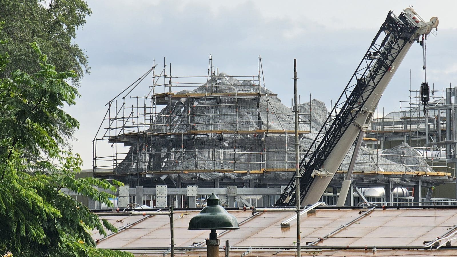 Construction site with scaffolding around a stone structure and a large crane on the right
