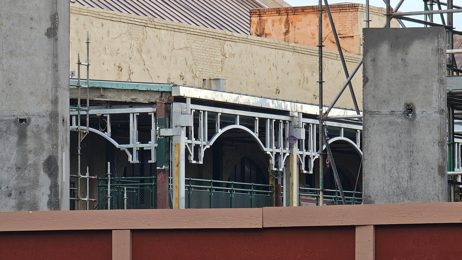 Construction site with scaffolding and concrete walls behind a brown wooden barrier at the bottom of the frame