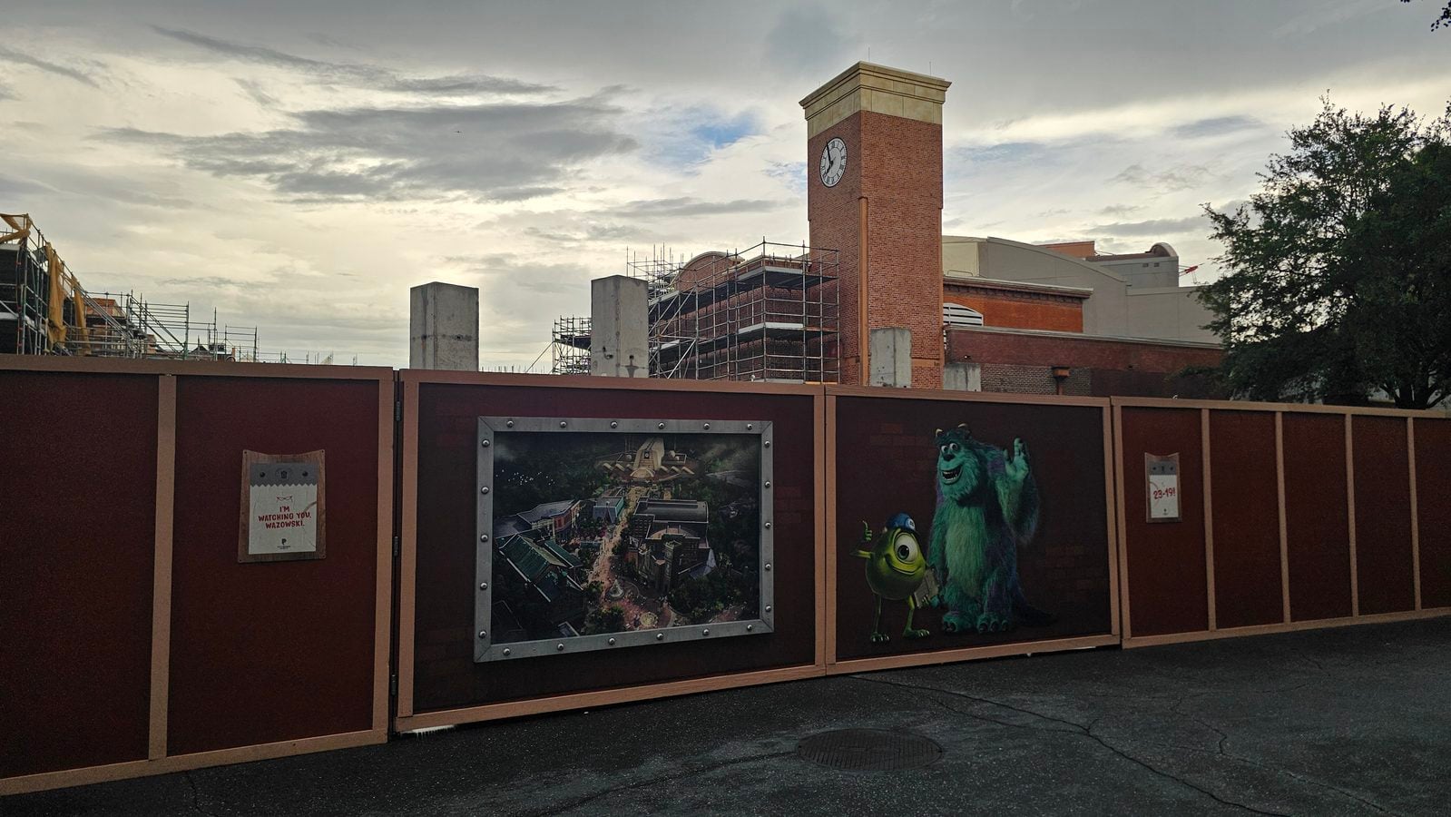 Construction site behind a brown framed fence with large posters including Mike and Sulley from Monsters Inc and a clock tower in the background