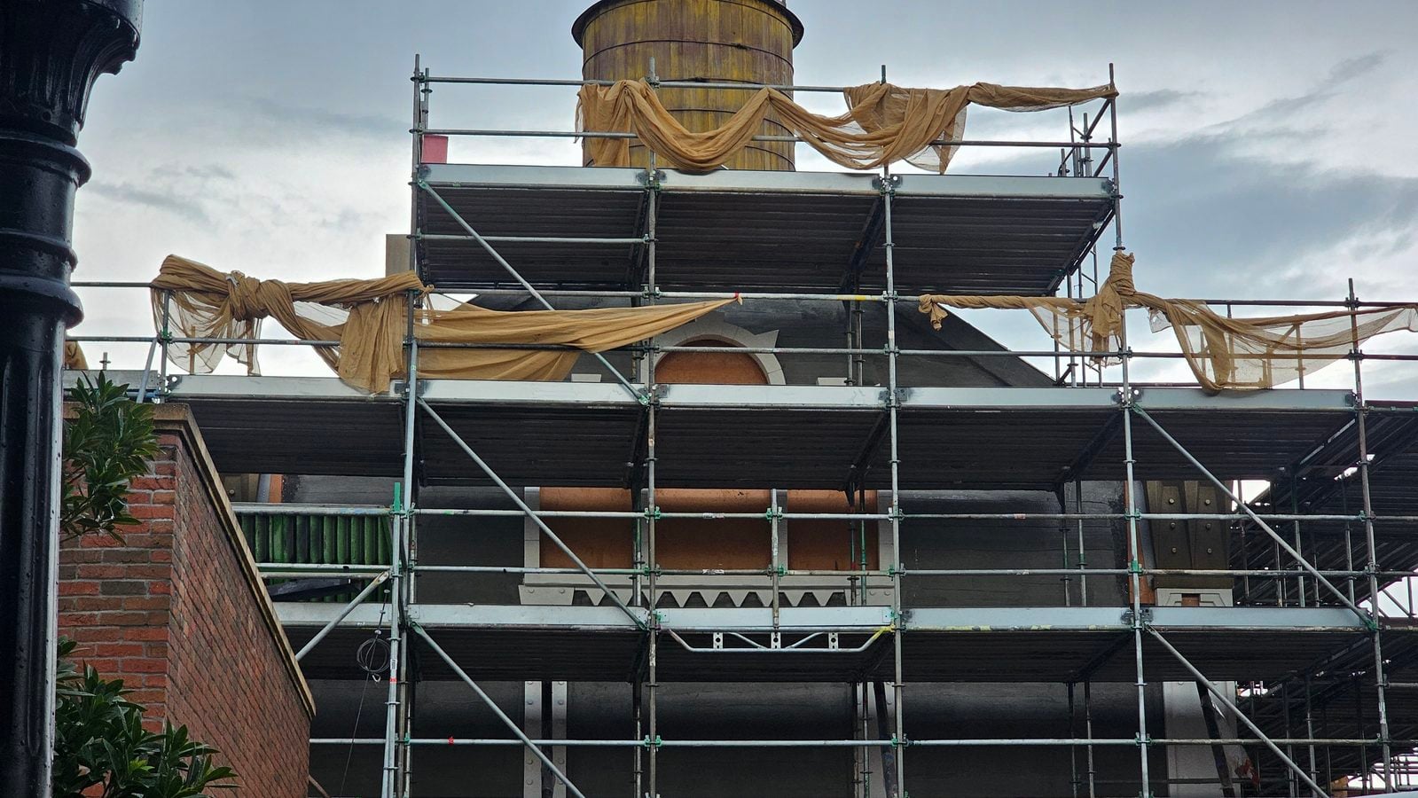 Construction scaffolding around a brick building with tan fabric draped along the rails and supports bacterial touch   informative