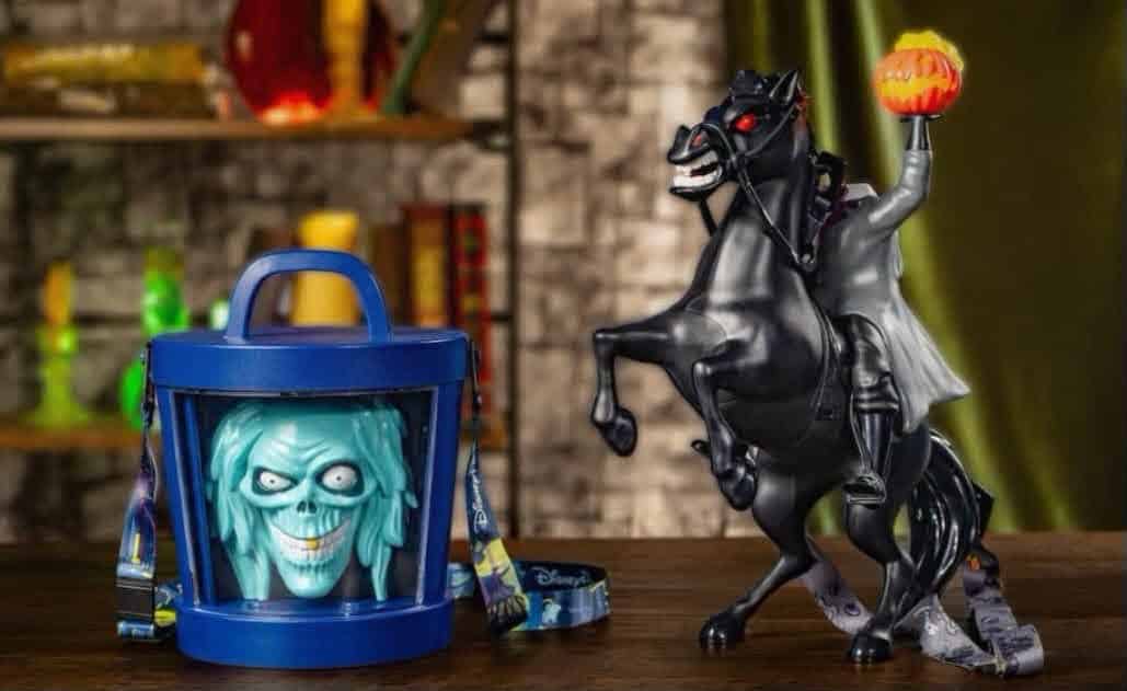 A blue plastic bucket toy with a glowing blue zombie face next to a black rearing horse figure holding a pumpkin lantern